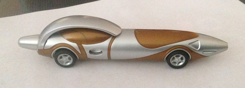 May include: A silver and brown toy car with a futuristic design. The car has a rounded front end and a long, sleek body.