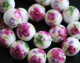 Può includere: Perle di ceramica bianca con un design floreale. I fiori sono viola e verdi con accenti dorati. Le perle sono rotonde e hanno una finitura liscia.