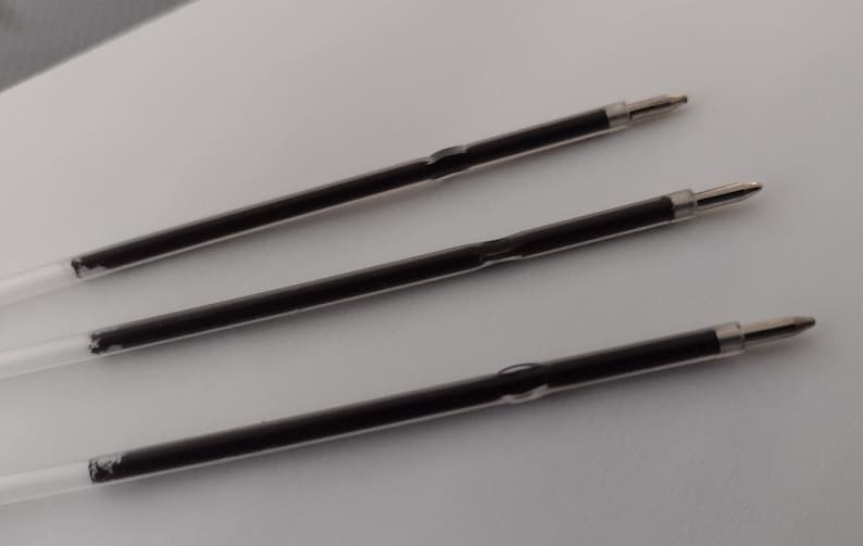 May include: Three black ink refills for a ballpoint pen. The refills are clear plastic tubes with black ink inside. The refills have a silver tip.