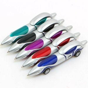 May include: Five silver and colored pens shaped like race cars. The pens have a silver body with a colored stripe and a small car design at the end. The colors are teal, black, purple, red, and blue.