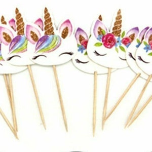 May include: A set of 10 unicorn cupcake toppers with gold glitter horns and colorful designs. The toppers are made of cardboard and have wooden sticks for inserting into cupcakes.