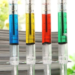 May include: Four plastic syringe pens with different colored inks: blue, yellow, red, and green. The pens are marked with measurements in millimeters.