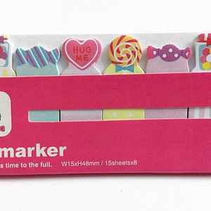 May include: A set of colorful sticky note flags with cute candy designs. The flags are arranged in a row and feature images of lollipops, candy jars, and a heart with the words "Hug Me". The text "stick marker" and "Composure creates time to the full. W15xH48mm / 15sheetsx8" is printed on the bottom of the package.