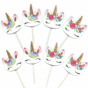 May include: Set of 7 unicorn cupcake toppers. Each topper features a white unicorn head with glitter, a rainbow mane, and a floral crown. The toppers are attached to wooden sticks.