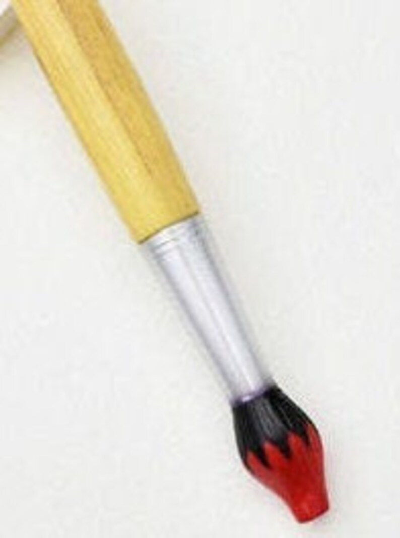 May include: A paintbrush with a light brown wooden handle, a silver ferrule, and a black and red bristle tip. The brush is angled against a white background, showcasing its design and construction.