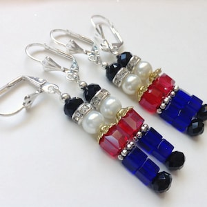Può includere: Un paio di orecchini pendenti d'argento con un design a forma di schiaccianoci. Gli orecchini sono realizzati con perline rosse, blu, nere, bianche e dorate.