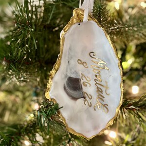 May include: Gold-painted oyster shell ornament with the text "To the future" and "8.26.22" written in gold calligraphy.