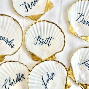 Plato para colocar tarjetas de lugar con forma de concha de vieira y caligrafía para decoración de mesa de boda costera