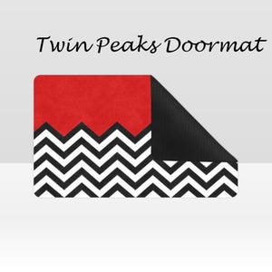 May include: Rectangular doormat with a red top section and a black and white zig-zag pattern. The text "Twin Peaks Doormat" is displayed at the top. The bottom right corner is black.