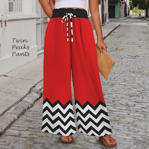 Puede incluir: Pantalones palazzo rojos con cintura negra y cordón blanco. La parte inferior de los pantalones presenta un patrón de zigzag en blanco y negro. El texto "Twin Peaks Pants" es visible en el lado izquierdo.