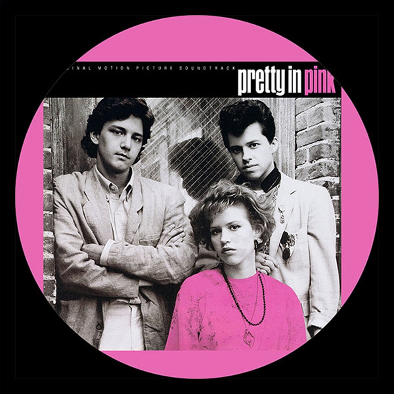 May include: Album cover for the "Pretty in Pink" soundtrack. The image features three people in front of a brick wall, framed by a pink circle. The title "pretty in pink" is in white text.