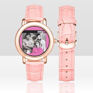 May include: A pink watch with a rose gold case and a matching pink faux-leather band. The watch face features a pink background with a black and white image of a band and the text "Pretty in Pink".
