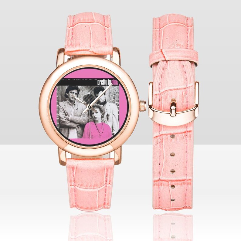 May include: A pink watch with a rose gold case and a matching pink faux-leather band. The watch face features a pink background with a black and white image of a band and the text "Pretty in Pink".