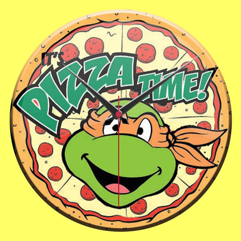 May include: Round wall clock featuring a pizza design with pepperoni and a smiling green turtle character wearing an orange mask. The clock face includes the text "It's Pizza Time!" in green and white. The clock hands are black.
