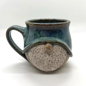 May include: A white ceramic mug with a black handle and the text "But First, Coffee" in a bold, black font. The mug is set against a blurred background, suggesting a cozy setting. The mug appears to be approximately 4 inches tall.