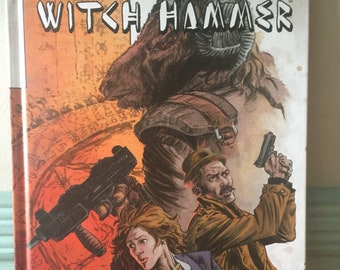 Könnte beinhalten: Ein Comic-Cover mit einer roten, orangefarbenen und braunen Illustration einer Gruppe von Menschen mit einer großen, pelzigen Kreatur. Der Titel des Comics lautet "Witch Hammer" und der Verlag ist "Aftershock".