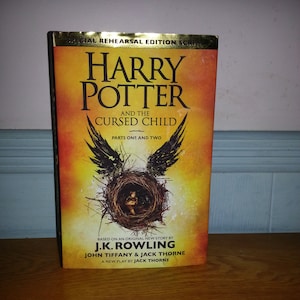 May include: A book cover for the play "Harry Potter and the Cursed Child" by J.K. Rowling, John Tiffany, and Jack Thorne. The cover features a dark brown nest with a golden glow, and the title is written in gold lettering.