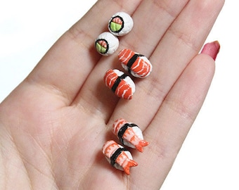 May include: A set of three miniature sushi earrings. The earrings are made of polymer clay and feature different types of sushi, including a maki roll, a nigiri with salmon, and a nigiri with shrimp. The earrings are a fun and unique way to show your love of sushi.