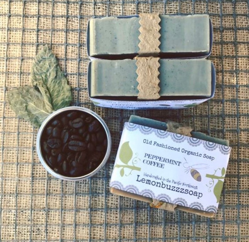 May include: Two bars of green peppermint coffee soap wrapped in brown paper with a white label that reads "Old Fashioned Organic Soap Peppermint Coffee Handcrafted in the Pacific Northwest Lemonbuzzzsoap". A small tin container filled with coffee beans is also in the image.