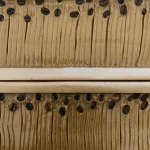 May include: Two rectangular bars of soap with a brown and beige swirl pattern. The soap is decorated with small brown coffee beans.