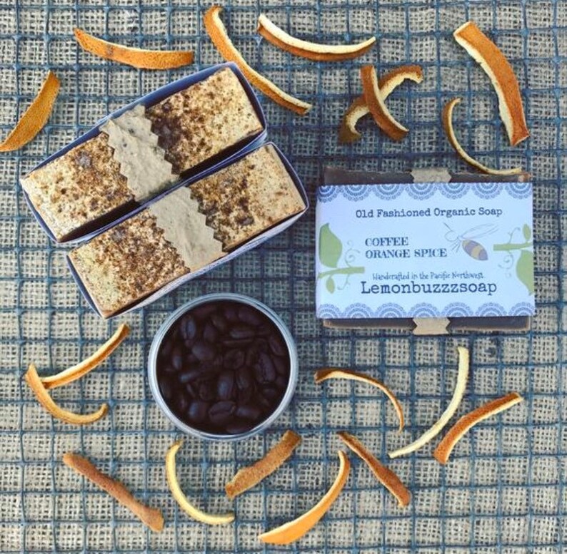 May include: Two bars of coffee and orange spice soap wrapped in brown paper and a tin of coffee beans. The soap is labeled "Old Fashioned Organic Soap, Coffee Orange Spice, Handcrafted in the Pacific Northwest, Lemonbuzzzsoap".