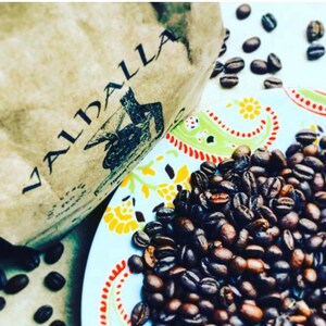 May include: A close-up of a bag of coffee beans labeled "Valhalla". The beans are scattered on a colorful patterned plate.