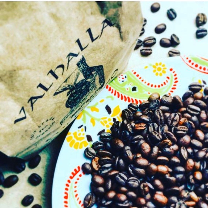 May include: A close-up of a bag of coffee beans labeled "Valhalla". The beans are scattered on a colorful patterned plate.
