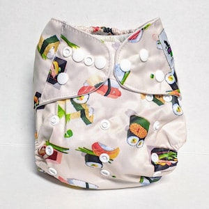 May include: A beige cloth diaper with a sushi print. The diaper has white snaps and is made of a soft, absorbent material.