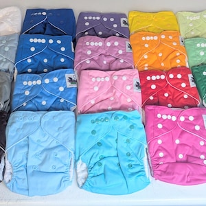 May include: A collection of colorful cloth diapers in various shades, including white, blue, purple, yellow, orange, green, pink, red, and black. Each diaper features snap closures and a white interior.