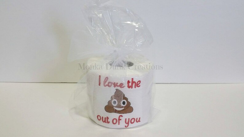 Op de afbeelding: Een witte toiletrol met een rood en bruin ontwerp met de tekst "I love the out of you" en een poep-emoji in het midden.