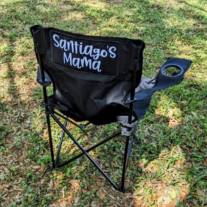 May include: Black folding camping chair with a cup holder and a white embroidered patch that says "Santiago's Mama".