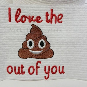 Op de afbeelding: Witte geborduurde keukendoek met rode tekst die "I love the out of you" zegt en een bruine poep-emoji.