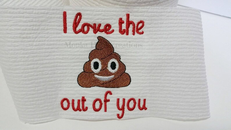 Op de afbeelding: Witte geborduurde keukendoek met rode tekst die "I love the out of you" zegt en een bruine poep-emoji.