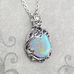 May include: Silver pendant necklace with an iridescent, oval stone. The stone is set in a decorative, leaf-like metal frame, hanging from a fine chain. The pendant has a vintage or fantasy style, with a subtle, colourful sheen.