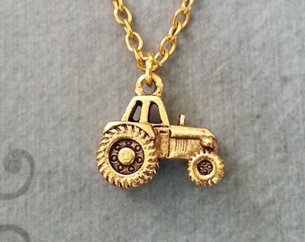 May include: Gold necklace featuring a small tractor charm. The tractor is detailed with a black grill and wheels.