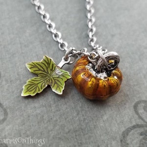 May include: A silver chain necklace with a small, orange and brown pumpkin charm and a green enamel leaf charm.