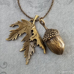 May include: A gold-toned necklace with an acorn and leaf pendant. The acorn is detailed with a textured cap and the leaf has a delicate, intricate design.