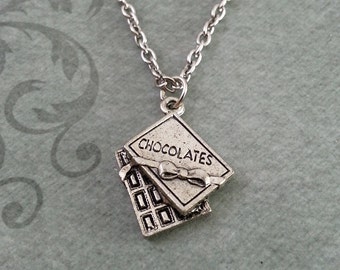 May include: A silver necklace with a charm of a chocolate bar with a bow and the word "CHOCOLATES" on it.
