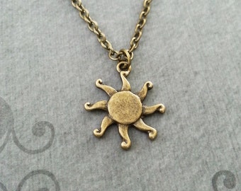 May include: A gold-toned necklace with a sun pendant. The sun has a circular center and eight rays that curve outward.