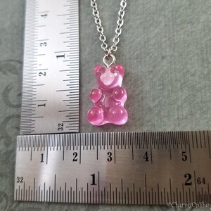 Puede incluir: Un collar con un dije de osito de gomita rosa y una cadena de plata. El dije mide aproximadamente 2,5 cm de alto y est&aacute; colgado de una regla.
