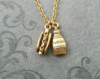 Op de afbeelding: Gouden ketting met een hotdog en een mosterd-flesje bedel. De mosterd-flesje bedel heeft het woord "MUSTARD" gegraveerd.