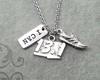 May include: Silver necklace with three charms: a running shoe, a sign that says "13.1", and a tag that says "I CAN".