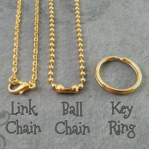 May include: Three gold chains, a link chain, a ball chain, and a key ring. The chains are hanging from the top of the image and the key ring is lying on the bottom of the image.