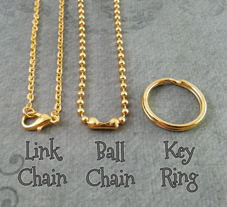 May include: Three gold chains, a link chain, a ball chain, and a key ring. The chains are hanging from the top of the image and the key ring is lying on the bottom of the image.