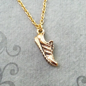 May include: A gold chain necklace with a gold running shoe pendant.