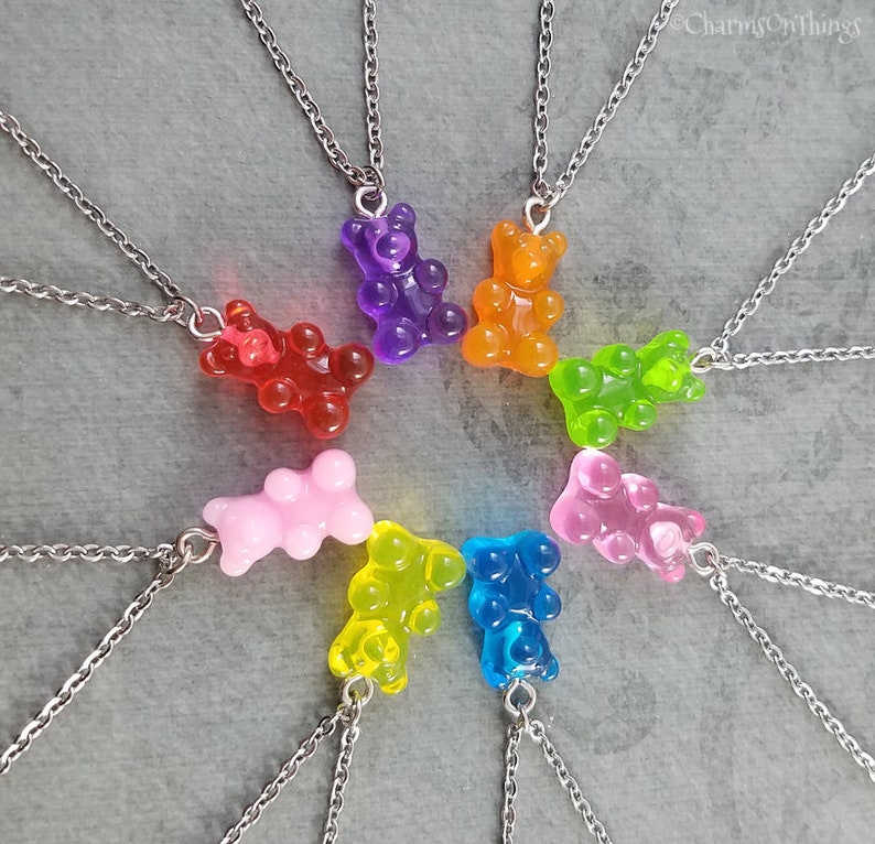 Puede incluir: Ocho collares de plata con dijes de ositos de gomita en diferentes colores: rojo, naranja, amarillo, verde, azul, rosa, morado y transparente. Los ositos de gomita tienen todos la forma de un oso de pie.