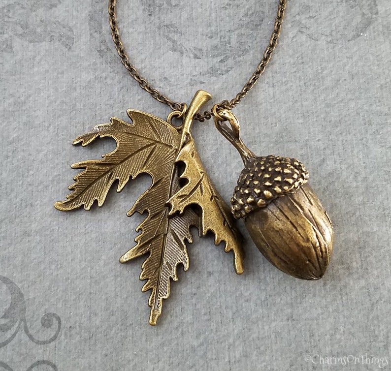 May include: A gold-toned necklace with an acorn and leaf pendant. The acorn is detailed with a textured cap and the leaf has a delicate, intricate design.