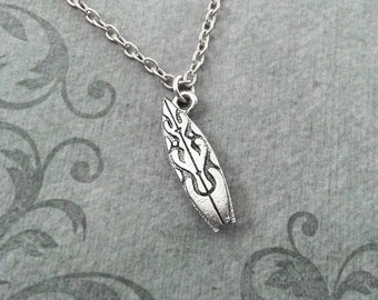 May include: A silver chain necklace with a silver surfboard pendant. The surfboard has a tribal design.