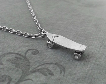 May include: A silver-colored skateboard pendant necklace. The pendant is a miniature skateboard with four wheels, attached to a delicate chain. The necklace is displayed on a gray surface.