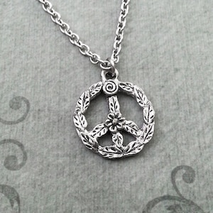 May include: A silver peace sign necklace with a floral design. The peace sign is surrounded by leaves and has a small flower in the center.